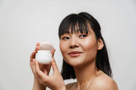 Young asian shirtless woman smiling while posing with face cream isolated over white backgroundの写真素材