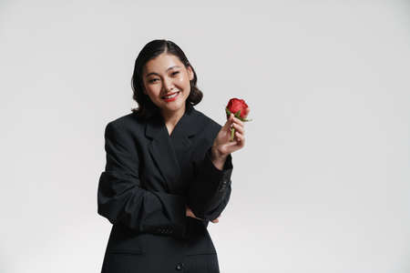 Brunette asian woman wearing jacket smiling and posing with rose isolated over white backgroundの写真素材