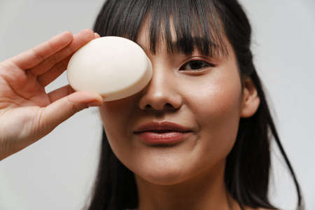 Young asian shirtless woman posing with piece of soap isolated over white backgroundの写真素材