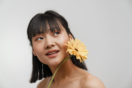 Young asian shirtless woman posing with gerbera flower isolated over white backgroundの写真素材