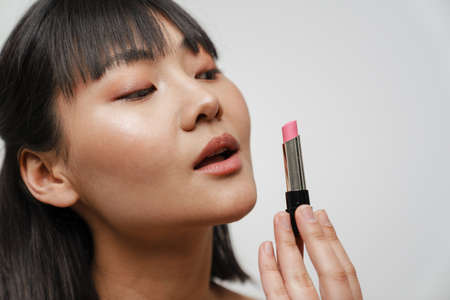 Young asian brunette woman posing and showing lipstick isolated over white background