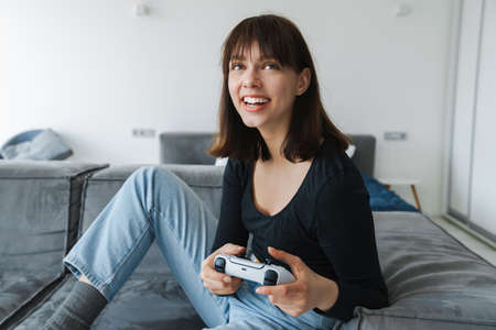 Happy young white woman holding joystick sitting on a couch at home