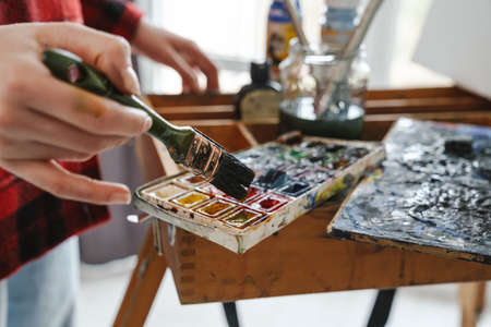 Close up of a female hand holding brush over paints on table indoors