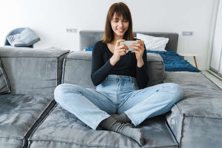 Smiling young woman using mobile phone while sitting on a couch at homeの写真素材