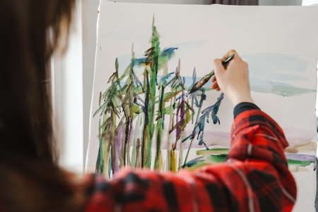 Young white woman painter holding paintbrush standing at the canvas indoors close upの写真素材