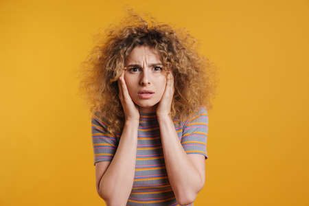 Shocked young casual woman with fizzy hairstyle standing over yellow wall backgroundの写真素材