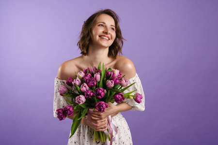 White young woman smiling while posing with tulips isolated over purple wallの写真素材