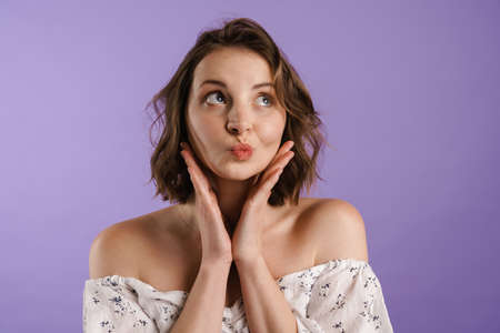 Puzzled young woman gesturing and looking aside isolated over purple wallの写真素材
