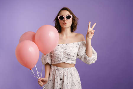 Excited young woman gesturing while posing with balloons isolated over purple wall