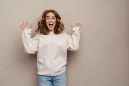 Young excited woman screaming and gesturing at camera isolated over grey backgroundの写真素材