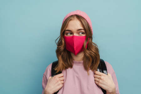 White student girl looking aside while posing in face mask isolated over blue backgroundの写真素材