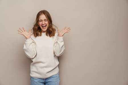 Young excited woman screaming and gesturing at camera isolated over grey background