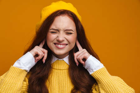 Happy young woman with long red hair in sweater and beret standing over yellow wall backgroundの写真素材