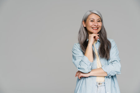 Mature white-haired woman smiling and looking at camera isolated over gray wall
