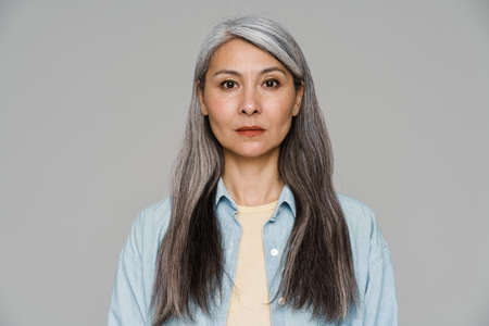 Mature white-haired woman posing and looking at camera isolated over gray wall