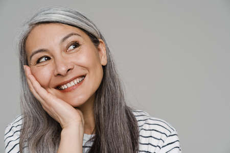 Mature white-haired woman smiling and looking aside isolated over gray wallの写真素材