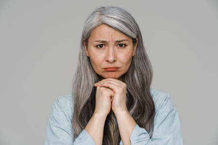 Displeased white-haired woman frowning and looking at camera isolated over gray wallの写真素材