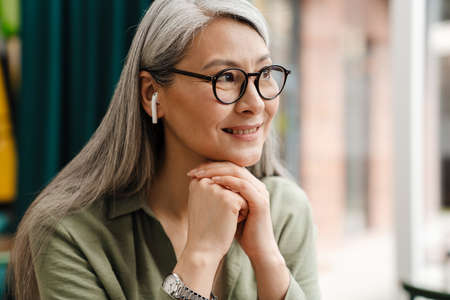 Mature grey woman smiling while listening music with earphones indoorsの写真素材