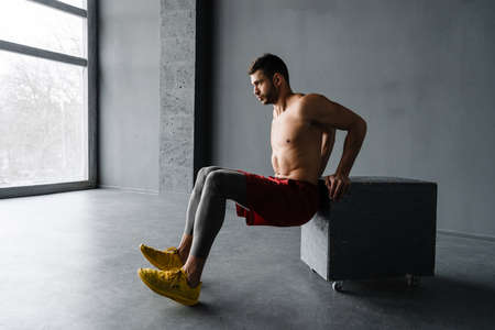 Young muscular shirtless sportsman exercising on a cube indoorsの写真素材