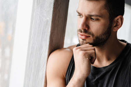 Young white puzzled sportsman looking out window indoorsの写真素材
