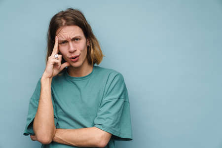 Young white man wearing t-shirt frowning while looking at camera isolated over blue wall