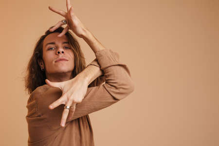 Young white man in shirt dancing and looking at camera isolated over beige wallの写真素材