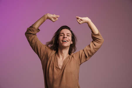 Young white man in shirt smiling and dancing on camera isolated over purple wallの写真素材