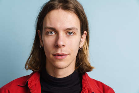Young white man wearing red jacket posing and looking at camera isolated over blue wall