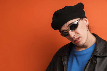 Young white man in sunglasses posing and looking at camera isolated over orange backgroundの写真素材