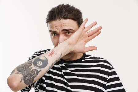 Young white man covering his face and looking at camera isolated over white backgroundの写真素材