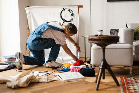 Young white man wearing overall working on craft rug at homeの写真素材