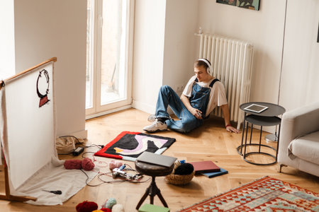 Young white man in headphones working on craft rug at homeの写真素材