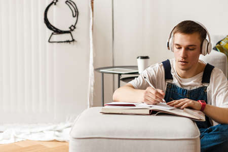 Young man in headphones writing down notes while working on craft rug at home