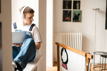 Young man in headphones using laptop while working on craft rug at homeの写真素材