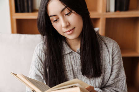 Young happy woman reading book while sitting on sofa in the living room