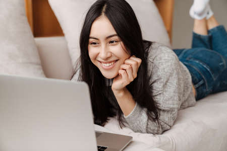 Happy pretty woman using laptop computer while relaxing on a couch at home