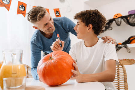 White father and son smiling while making Halloween pumpkin together at home