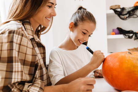 White mother and daughter smiling while making Halloween pumpkin together at homeの写真素材