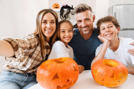 White family smiling while taking selfie photo with Halloween pumpkins at homeの写真素材