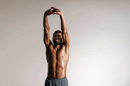Black shirtless sportsman doing stretching exercise while working out isolated over white backgroundの写真素材
