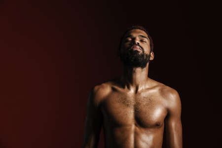 Black shirtless sportsman posing on camera with eyes closed isolated red white backgroundの写真素材