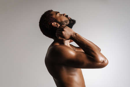 Black shirtless sportsman doing stretching exercise while working out isolated over white backgroundの写真素材