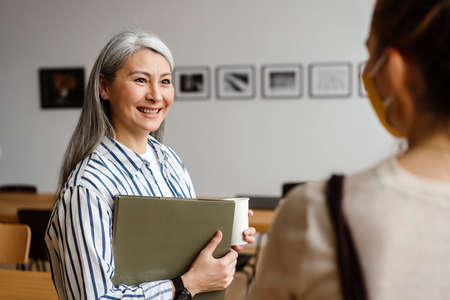 Two employee standing in social distance wearing face mask talking in the officeの写真素材