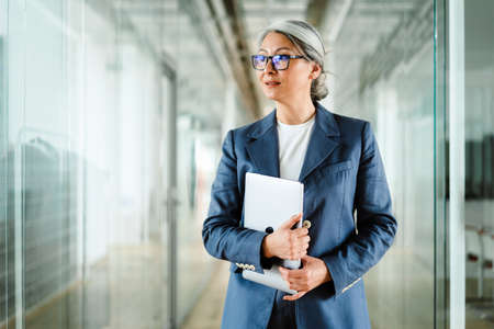 Focused white-haired mature businesswoman posing with laptop indoors