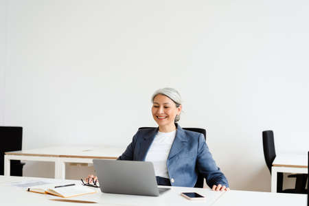 Cheerful white-haired businesswoman smiling while working with laptop in office