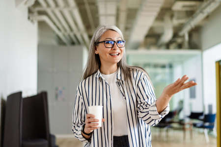 Happy white-haired mature woman holding copyspace while drinking coffee indoorsの写真素材