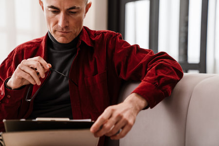 Handsome serious man working with papers while sitting on couch at homeの写真素材