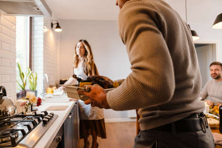 White couple cooking turkey for thanksgiving dinner with their friends at homeの写真素材