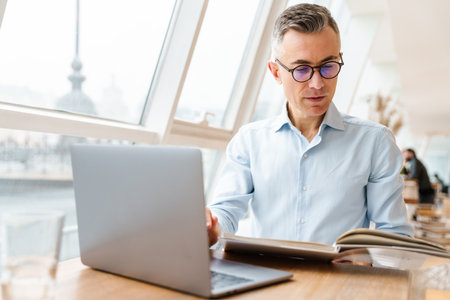 Confident handsome businessman in smart clothes working on laptop computer while sitting in the cafe...