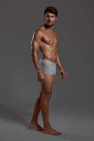 Young good-looking focused european athletic man. Side view of bearded man with dark hair and naked sportive torso. Isolated on dark gray background. Studio shoot. Copy spaceの写真素材